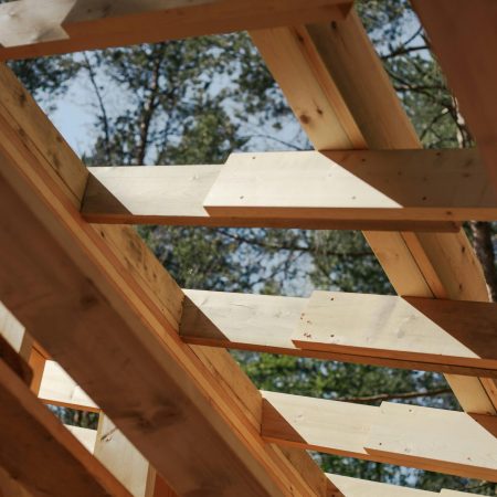 Close-up view of wooden beams forming a house roof structure against a sky background.